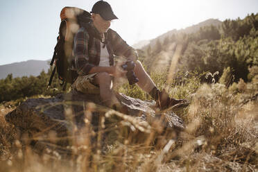 Hiker looking at pictures on digital camera during hiking. Senior man taking a break on a hike to looking at photos. - JLPSF17343