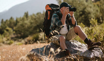 Älterer Mann beim Fotografieren mit einer Digitalkamera. Rentner sitzt auf einem Felsen und fotografiert beim Wandern. - JLPSF17344