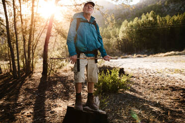 Älterer Mann auf Wandertour, der auf einem Felsen steht und den Berggipfel betrachtet. Älterer Mann, der eine Pause auf einem Bergpfad macht, um die schöne Natur zu bewundern. - JLPSF17352