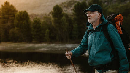 Älterer Mann, der an einem Fluss auf einem Bergpfad spazieren geht. Ein fitter reifer Mann, der einen Rucksack trägt, wandert in der Natur. - JLPSF17357