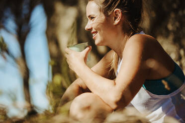Lächelnde junge Frau trinkt Kaffee beim Trekking. Sportliche Frau ruht sich beim Wandern aus. - JLPSF17359