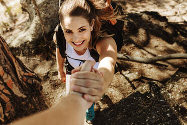 Closeup of man helping woman to climb a rock. Female climbing a rock with help from a male friend. - JLPSF17364