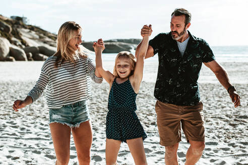 Ein Paar, das seine Tochter an der Hand hält und am Strand spielt, ein Mädchen, das sich mit seinen Eltern im Sommerurlaub amüsiert. - JLPSF17394