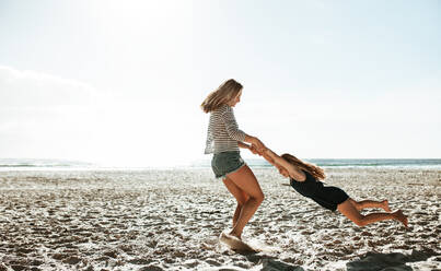 Mutter und Tochter vergnügen sich am Strand; Frau hält das Mädchen an der Hand und dreht es am Strand - JLPSF17396