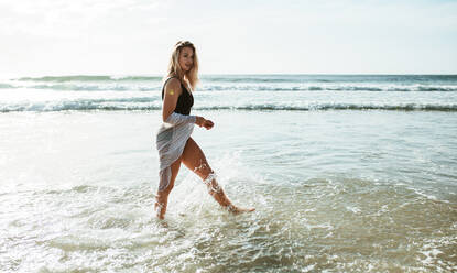 Frau, die am Strand im Wasser spazieren geht. Schöne Frau in Badekleidung, die am Meeresufer spazieren geht. - JLPSF17398