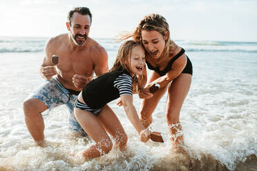 Eine Familie, die Eisbonbons in der Hand hält und im Meerwasser spielt, Vater, Mutter und Tochter, die ein Sommerwochenende am Strand genießen. - JLPSF17399