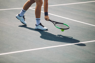 Cropped shot of sportsperson on tennis court picking the ball with racket. Male tennis player pick up the ball on hard court. - JLPSF17460