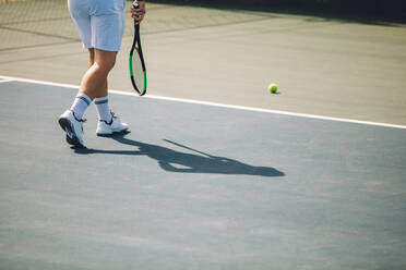 Ausschnitt eines männlichen Tennisspielers, der auf einem Hartplatz auf den Ball zugeht. Ein Mann in weißer Sportkleidung spielt Tennis auf einem Hartplatz. - JLPSF17461