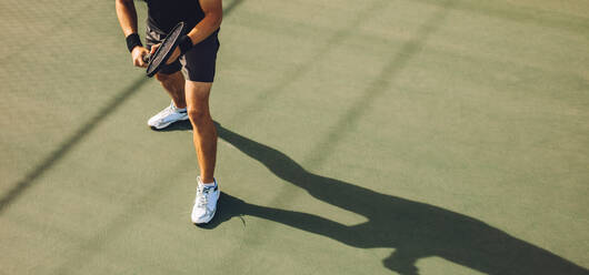 Tennis player playing tennis on hard court. Young man in sports wear standing on hard tennis court ready to return the serve during a game. - JLPSF17462