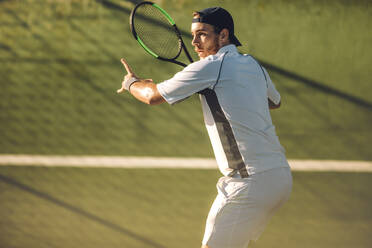 Fit junger Tennisspieler, der den Aufschlag mit einer kraftvollen Vorhand zurückschlägt. Tennisspieler, der ein Match auf einem Hartplatz spielt. - JLPSF17485