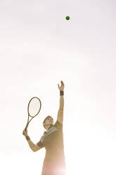 Männlicher Tennisspieler, der an einem sonnigen Tag einen Ball zum Aufschlag hochwirft. Tennisspieler, der in einem Spiel einen Ball aufschlägt. - JLPSF17502