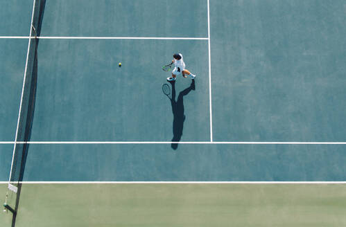 Luftaufnahme eines jungen männlichen Tennisspielers, der auf einem Hartplatz geht, um den Ball zu holen. Professioneller Tennisspieler auf einem Clubplatz. - JLPSF17513
