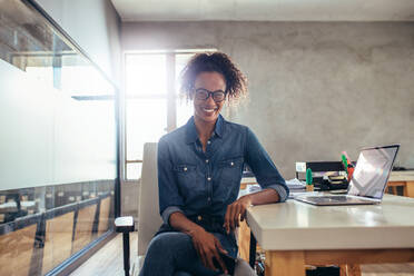 Positive young businesswoman sitting at office desk. Young african female at work. - JLPSF17533