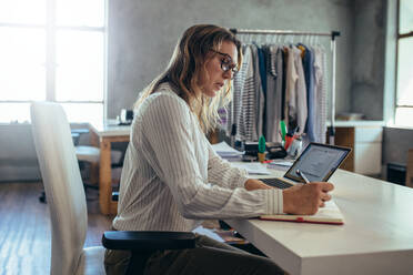 Frau in Freizeitkleidung schreibt in ihr Tagebuch mit Laptop auf dem Schreibtisch. E-Commerce Unternehmerin nimmt Online-Bestellungen entgegen. - JLPSF17551