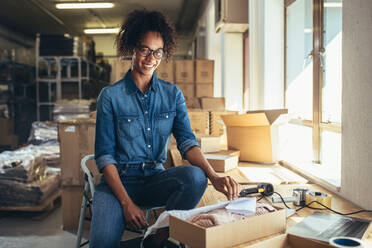 Lächelnde junge Frau, die das Produkt für den Versand an den Kunden verpackt. Online-Unternehmerin bei der Arbeit im Büro. - JLPSF17574