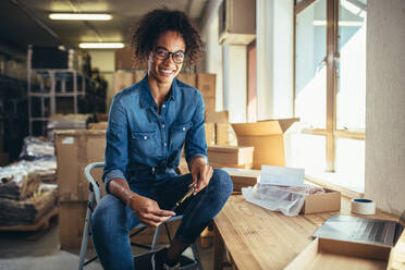 Lächelnde junge Frau, die an ihrem Arbeitsplatz sitzt. Selbstbewusste Online-Unternehmerin, die in die Kamera schaut und lächelt. - JLPSF17575