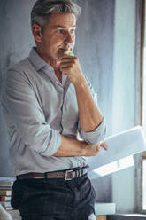 Mature businessman standing in office and thinking. Businessman in casuals at his office looking pensive. - JLPSF17603