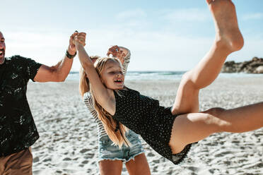 Eltern, die ihre Tochter am Strand in die Luft schwingen. Glückliche Familie, die bei einem Strandspaziergang verspielt ist - JLPSF17608