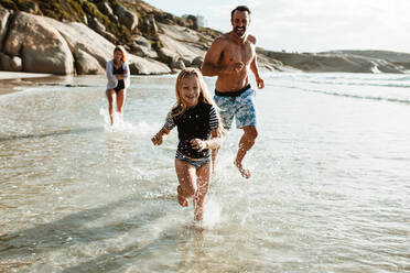 Familie beim Spielen am Strand. Mädchen läuft mit Vater und Mutter im Wasser am Strand. - JLPSF17612