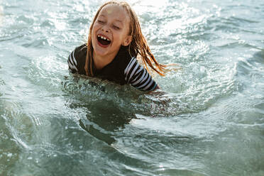 Aufgeregtes Mädchen beim Schwimmen im Meerwasser. Junges Mädchen sitzt im Meerwasser und lächelt. - JLPSF17617