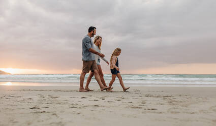 Family of three walking together on a beach vacation. Couple with their daughter on evening walk along the beach. - JLPSF17622