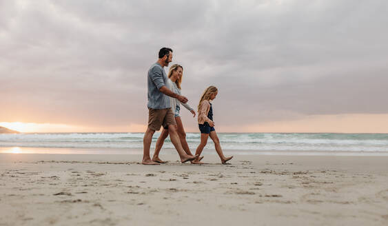Eine dreiköpfige Familie, die gemeinsam am Strand spazieren geht. Ein Ehepaar mit seiner Tochter bei einem Abendspaziergang am Strand. - JLPSF17622