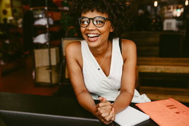 Smiling young african woman sitting in the cafe. Afro american woman sitting at a restaurant table and smiling. - JLPSF17623