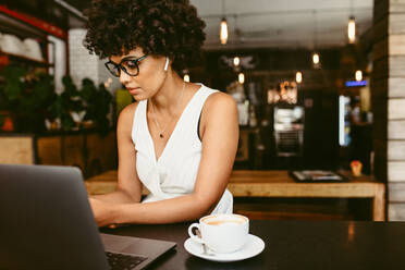 Afrikanische Frau sitzt im Café mit Laptop und Tasse Kaffee auf dem Tisch. Junge Frau arbeitet in einem Café. - JLPSF17629