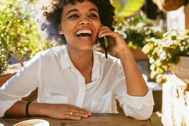 Schöne und glückliche Frau im Gespräch über Handy im Café. Afrikanische Frau im Café mit ihrem Handy. - JLPSF17639
