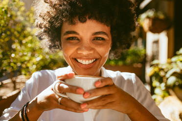 Close up of a woman with a cup of coffee sitting at cafe. African female having a coffee at outdoor coffeeshop. - JLPSF17640