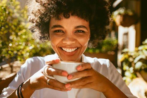 Nahaufnahme einer Frau mit einer Tasse Kaffee im Café sitzend. Afrikanische Frau trinkt einen Kaffee in einem Coffeeshop. - JLPSF17640
