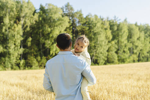 Vater trägt Tochter im Feld an einem sonnigen Tag - SEAF01379