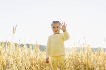 Glückliches süßes Mädchen gestikulierend und stehend im Feld an einem sonnigen Tag - SEAF01384