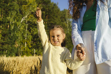 Mädchen hält Hände mit Mutter und steht auf einem Feld an einem sonnigen Tag - SEAF01386
