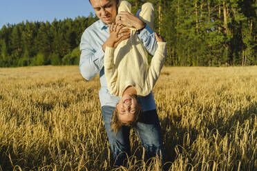Verspielter Mann trägt glückliche Tochter kopfüber auf einem Feld - SEAF01393