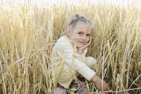 Smiling girl crouching amidst plants in field - SEAF01398