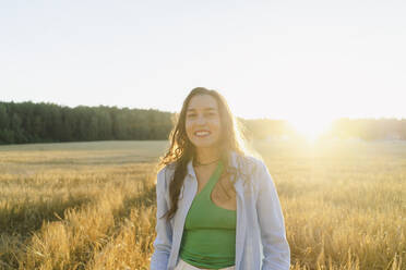 Glückliche Frau steht auf einem Feld bei Sonnenuntergang - SEAF01413