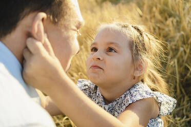 Lächelndes Mädchen spielt mit Vater auf einem Feld bei Sonnenuntergang - SEAF01416