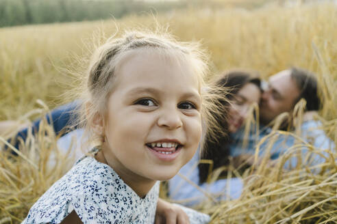 Glückliches Mädchen mit Mutter und Vater auf einem Feld im Hintergrund liegend - SEAF01430
