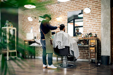 Rückansicht männlicher Friseur mit Kamm, der das Haar eines nicht erkennbaren Kunden bürstet, während er eine Frisur in einem modernen Friseursalon macht - ADSF39932
