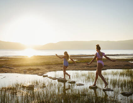 Schwestern (12-13, 14-15), die bei Sonnenaufgang auf Trittsteinen im See laufen - TETF01826