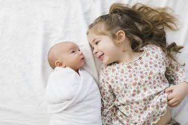Overhead view of girl (2-3) smiling to baby brother (0-1 months) on bed - TETF01831