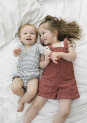 Draufsicht auf Bruder (12-17 Monate) und Schwester (2-3) beim Kuscheln im Bett - TETF01833