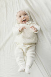 Overhead view of baby boy (2-5 months) in white outfit lying on bed - TETF01834