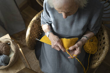 Ältere Frau strickt auf einem Stuhl zu Hause - SVKF00652