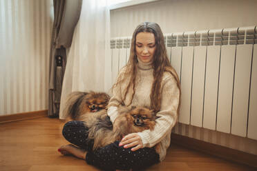Lächelnde Frau mit Hunden, die sich zu Hause an den Heizkörper lehnen - MDOF00123