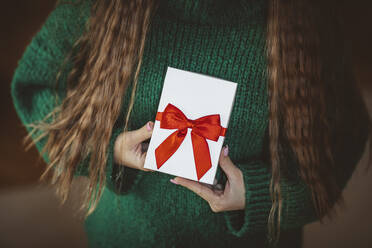 Frau mit grünem Pullover hält Geschenk zu Hause - MDOF00132