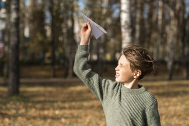 Junge spielt mit Papierflugzeug im Park - ANAF00257