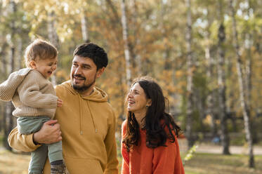 Happy man carrying son standing by woman in park - ANAF00259