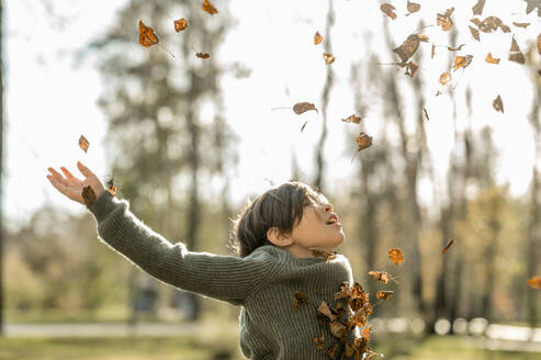 Verspielter Junge wirft trockene Blätter im Park - ANAF00273